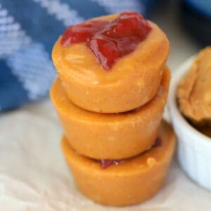 Sugar free peanut butter bombs stacked on top of each other next to a bowl with peanut butter and a blue kitchen towel.