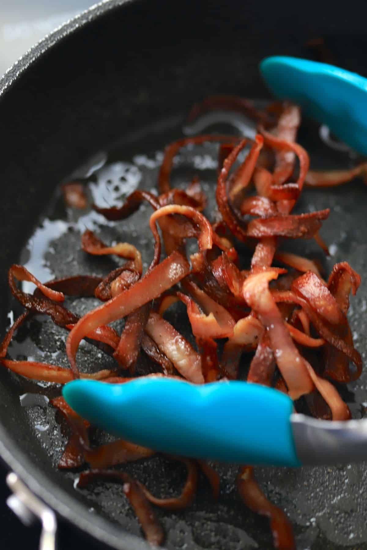 frying mortadella ribbons in a frying pan with tongs.