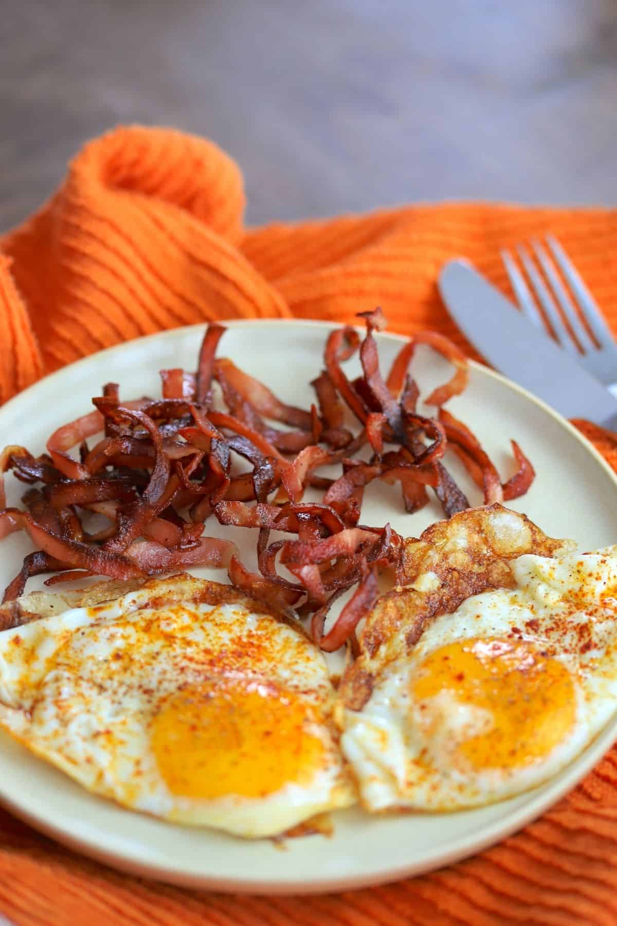 fried mortadella with eggs, cutlery on an orange napkin.