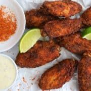 tajin chicken wings on parchment paper with lime wedges and dipping sauce.