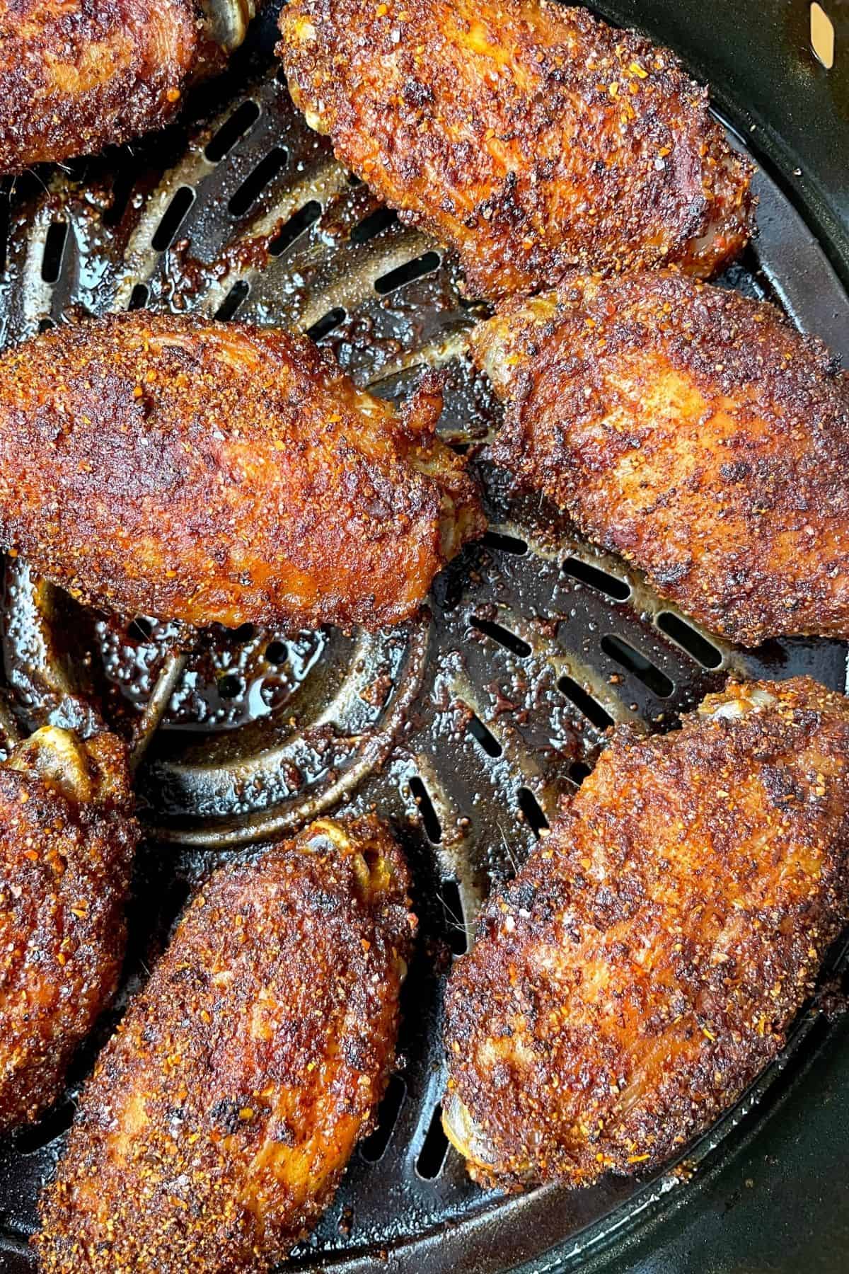 Cooked chicken wings in air fryer basket.