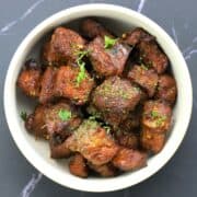 white bowl with cubes of steak bites topped with chopped parsley.