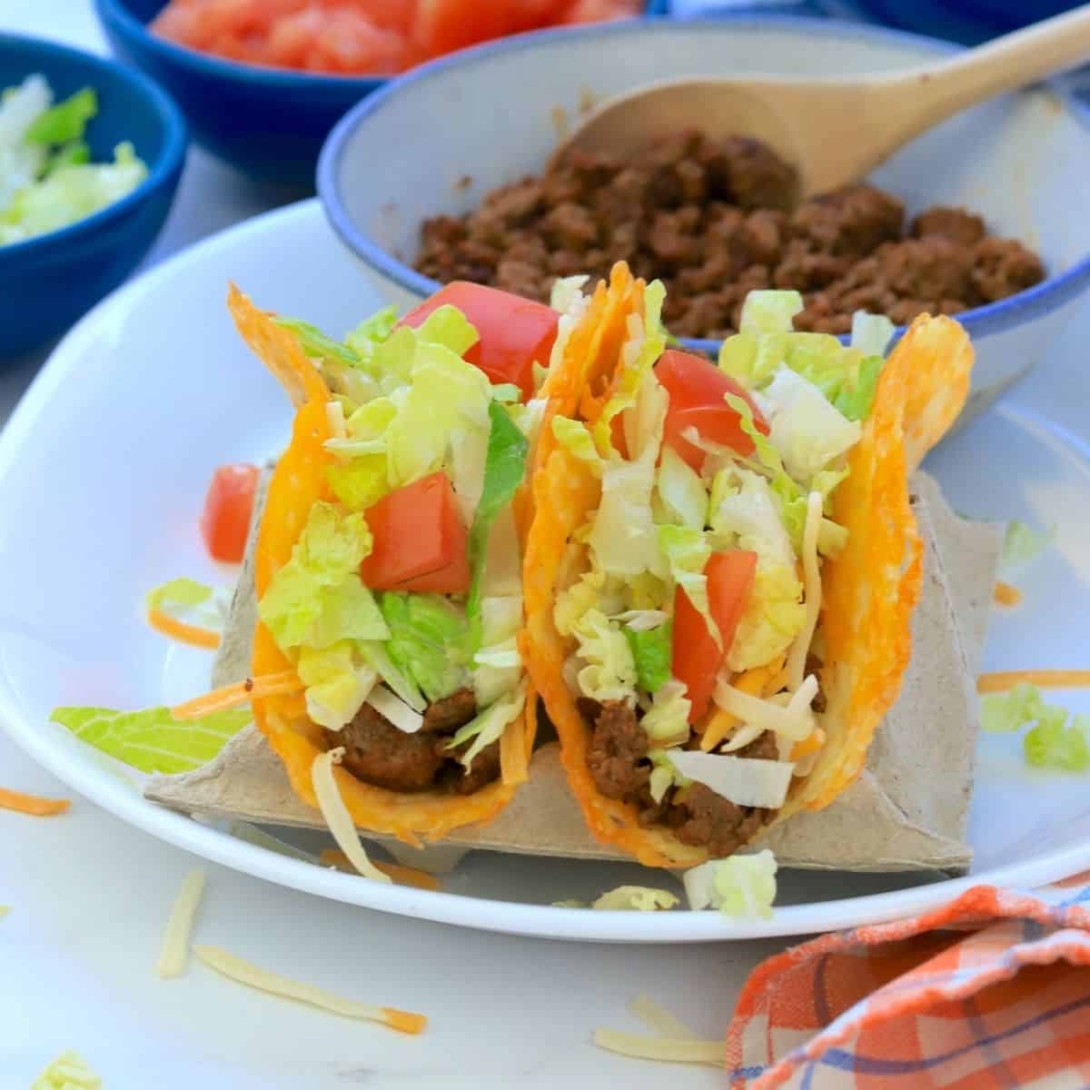 2 keto beef tacos with toppings and side dishes of ground beef, diced tomatoes, shredded lettuce and cheese.