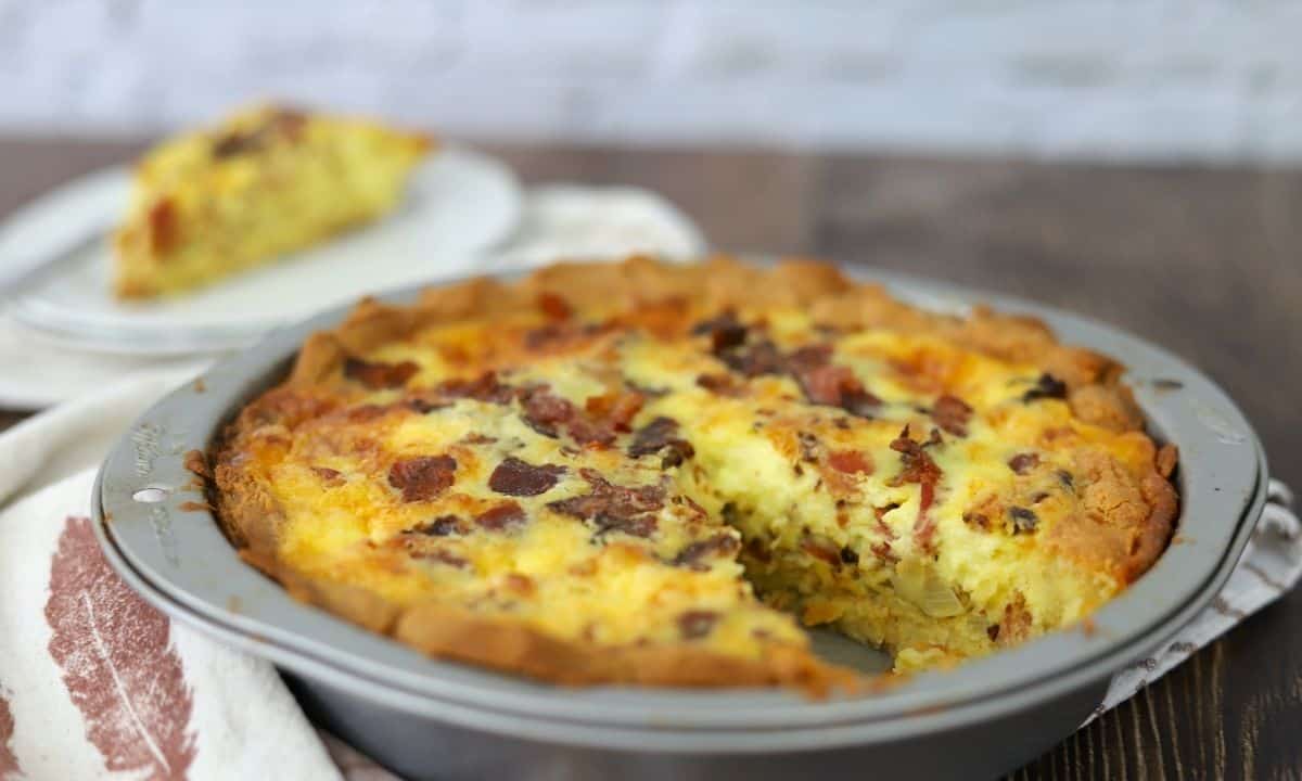 close up of keto quiche lorraine in pie pan with a slice out of focus.