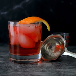 negroni cocktail with strainer and orange wedge.