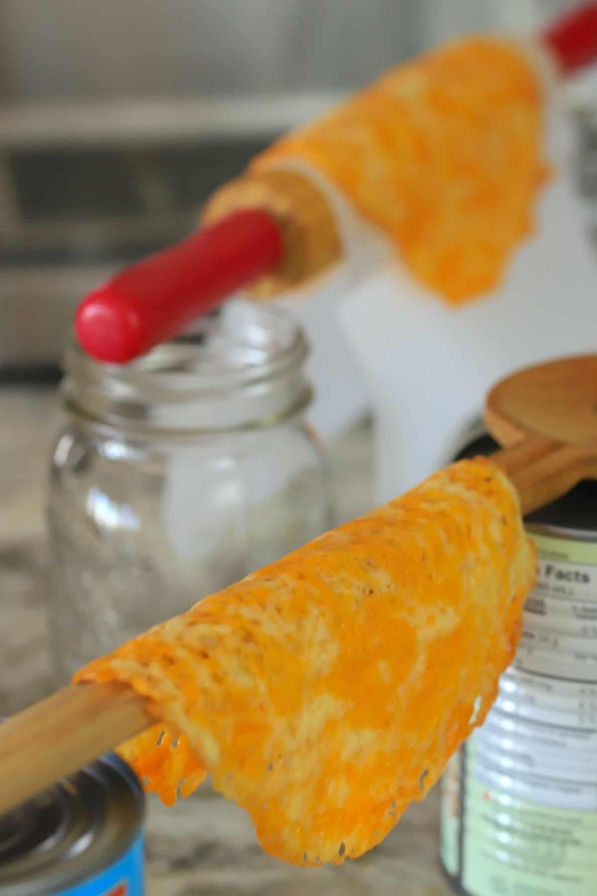 2 cheese taco shells resting on rolling pin and wooden spoon.