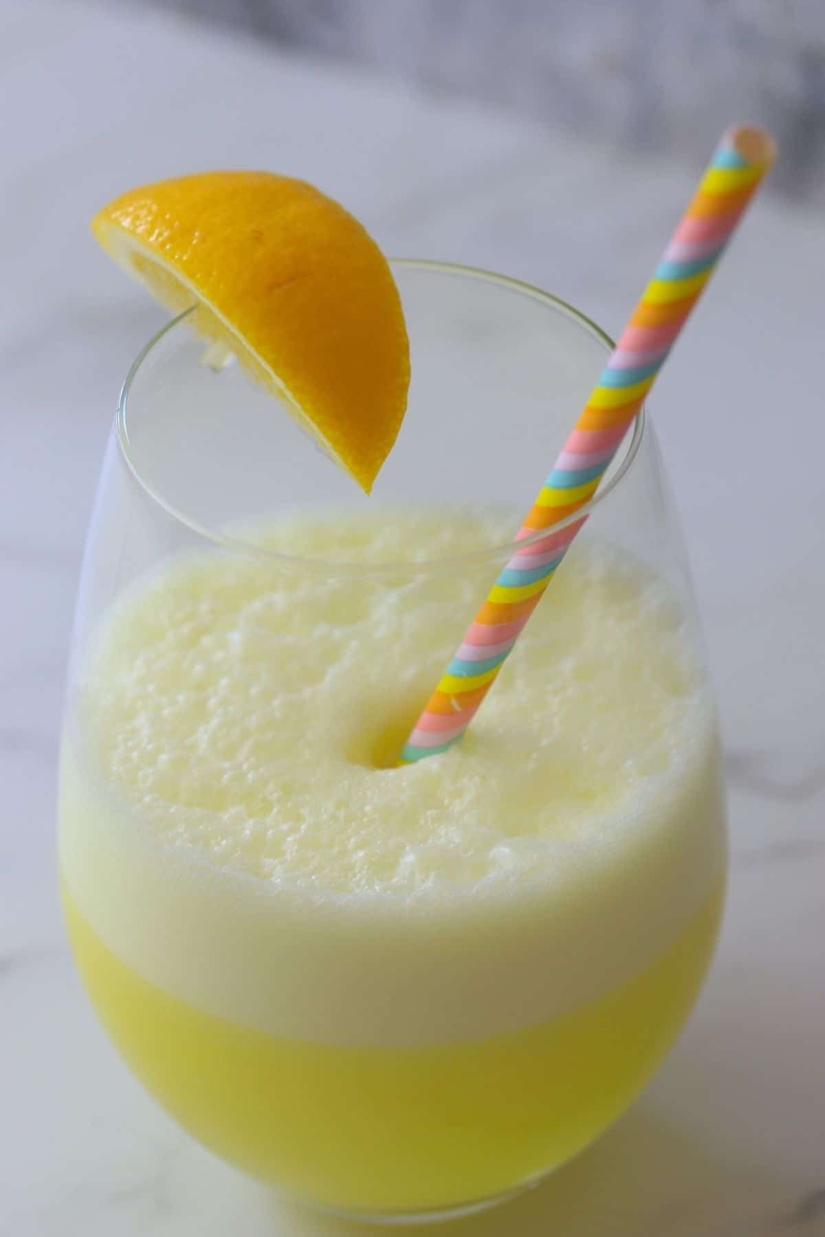 a glass with a foamy lemonade electrolyte smoothie with a lemon wedge and a straw.