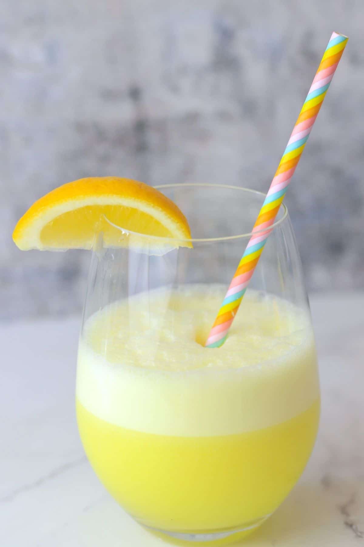 a glass with a foamy lemonade electrolyte smoothie with a lemon wedge and a straw.