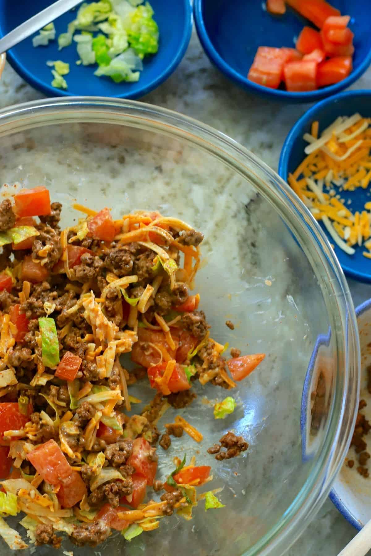 glass bowl with taco salad and side bowls with lettuce, tomato and cheddar.