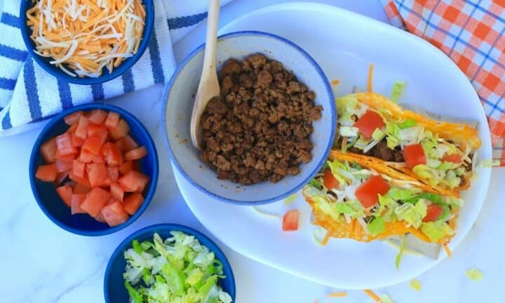 2 keto beef tacos with toppings and side dishes of ground beef, diced tomatoes, shredded lettuce and cheese.