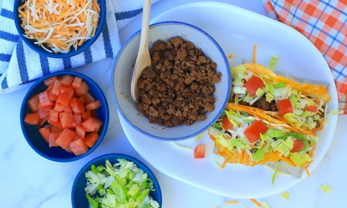 2 keto beef tacos with toppings and side dishes of ground beef, diced tomatoes, shredded lettuce and cheese.