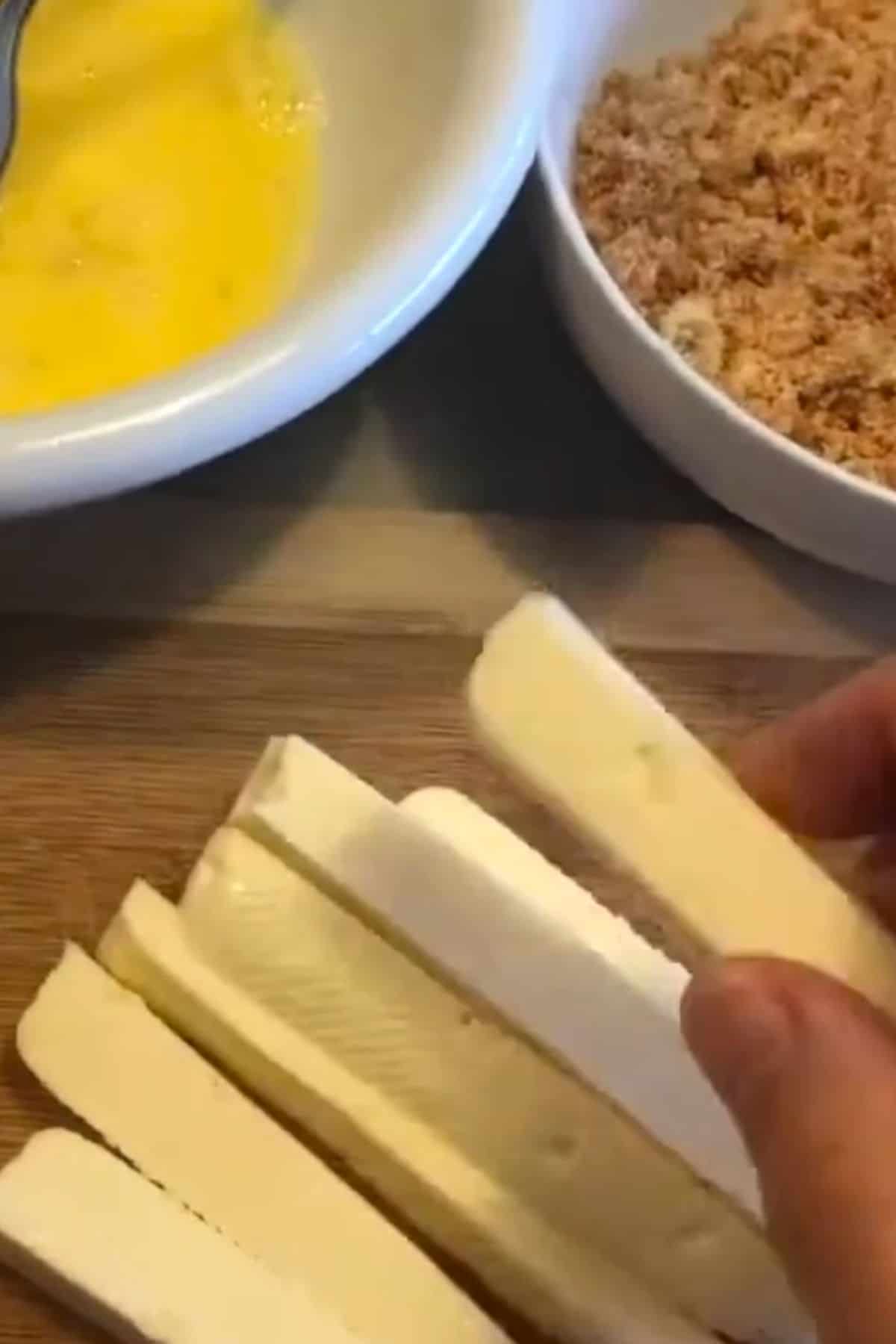 keto halloumi fry sticks next to a bowl of egg and breadcrumbs.