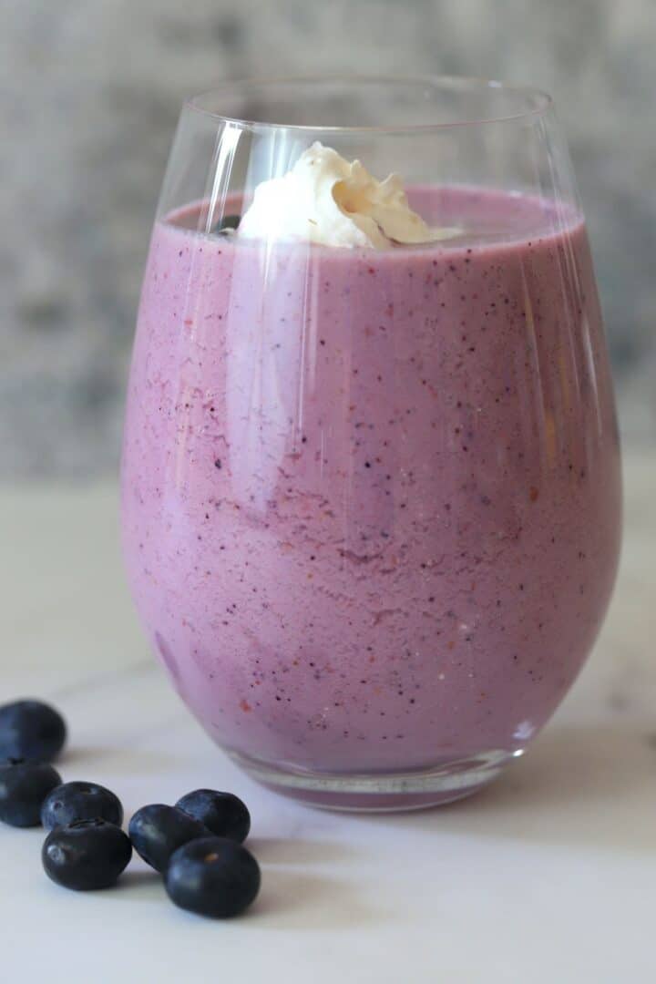 low carb berry smoothie in a clear glass next to blueberries.