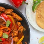 skillet with low carb chicken fajita and side of tortillas, lime wedges and red pepper.