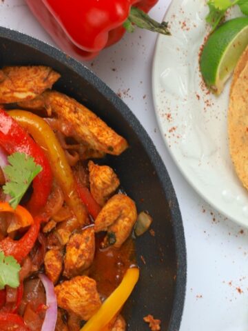 skillet with low carb chicken fajita and side of tortillas, lime wedges and red pepper.