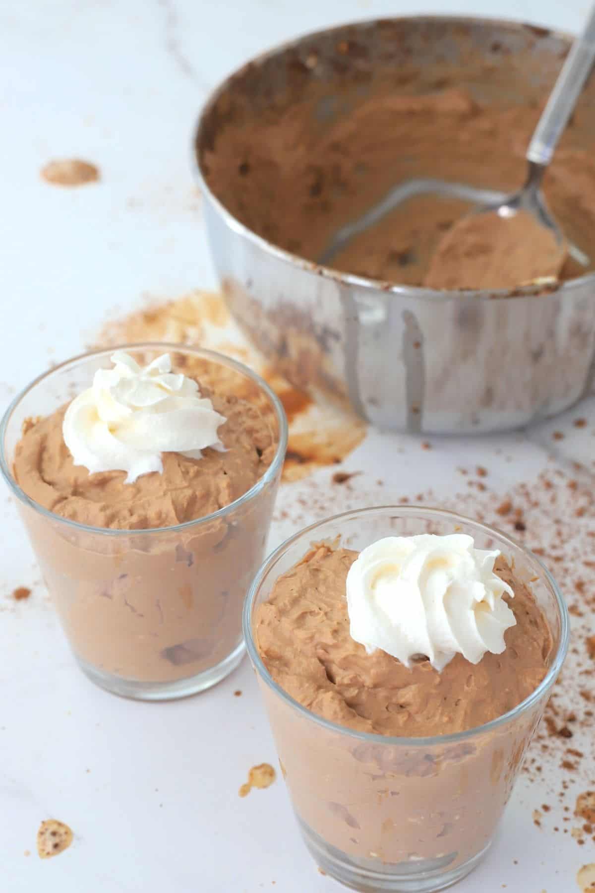 two low carb chocolate mousse dessert next to creamy chocolate in a bowl.