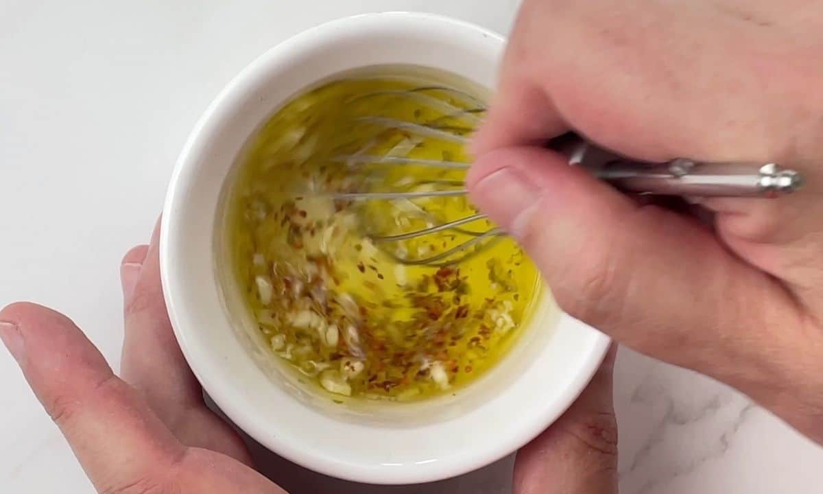 stirring olive oil mixture in a white bowl.