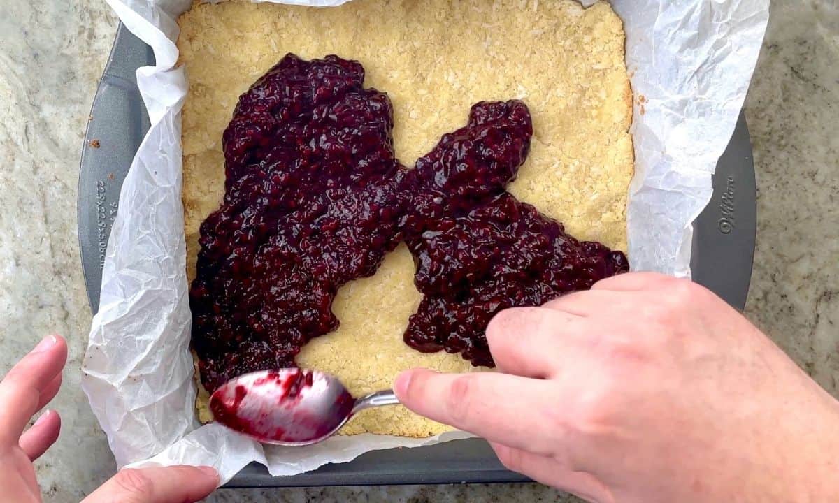 spreading the blackberry sauce onto the crust with a spoon.