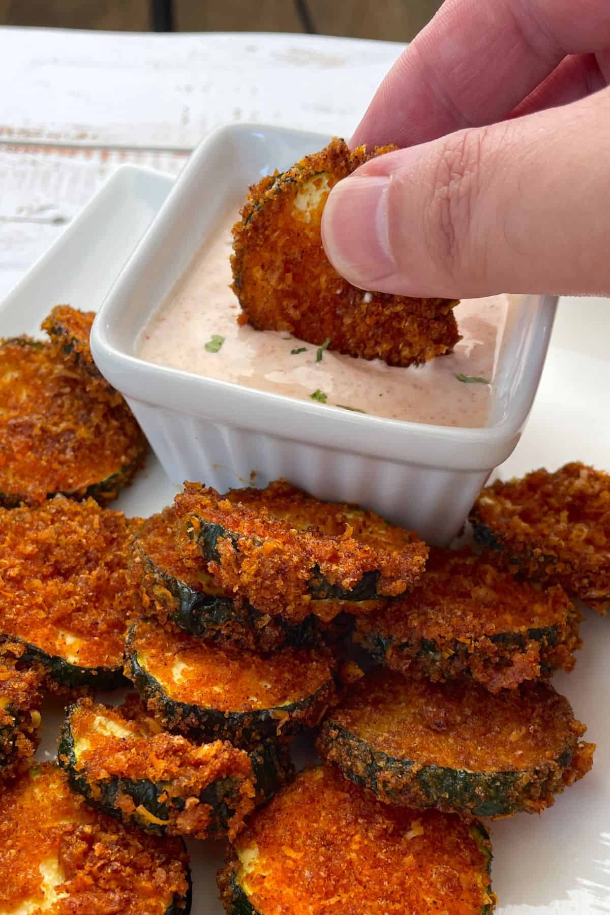dipping an air fried zucchini keto chip into a bowl of dip.