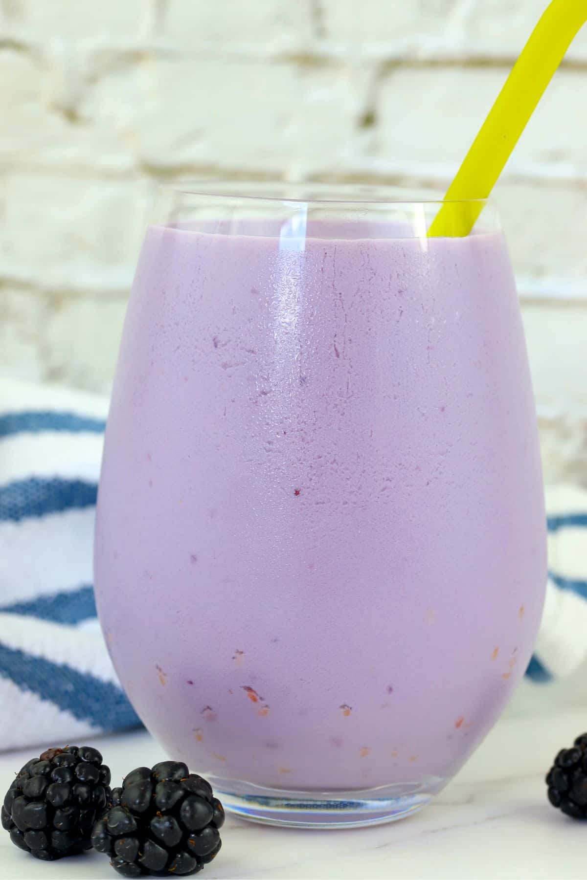 low carb blackberry smoothie with a yellow straw and fresh blackberries on the side.
