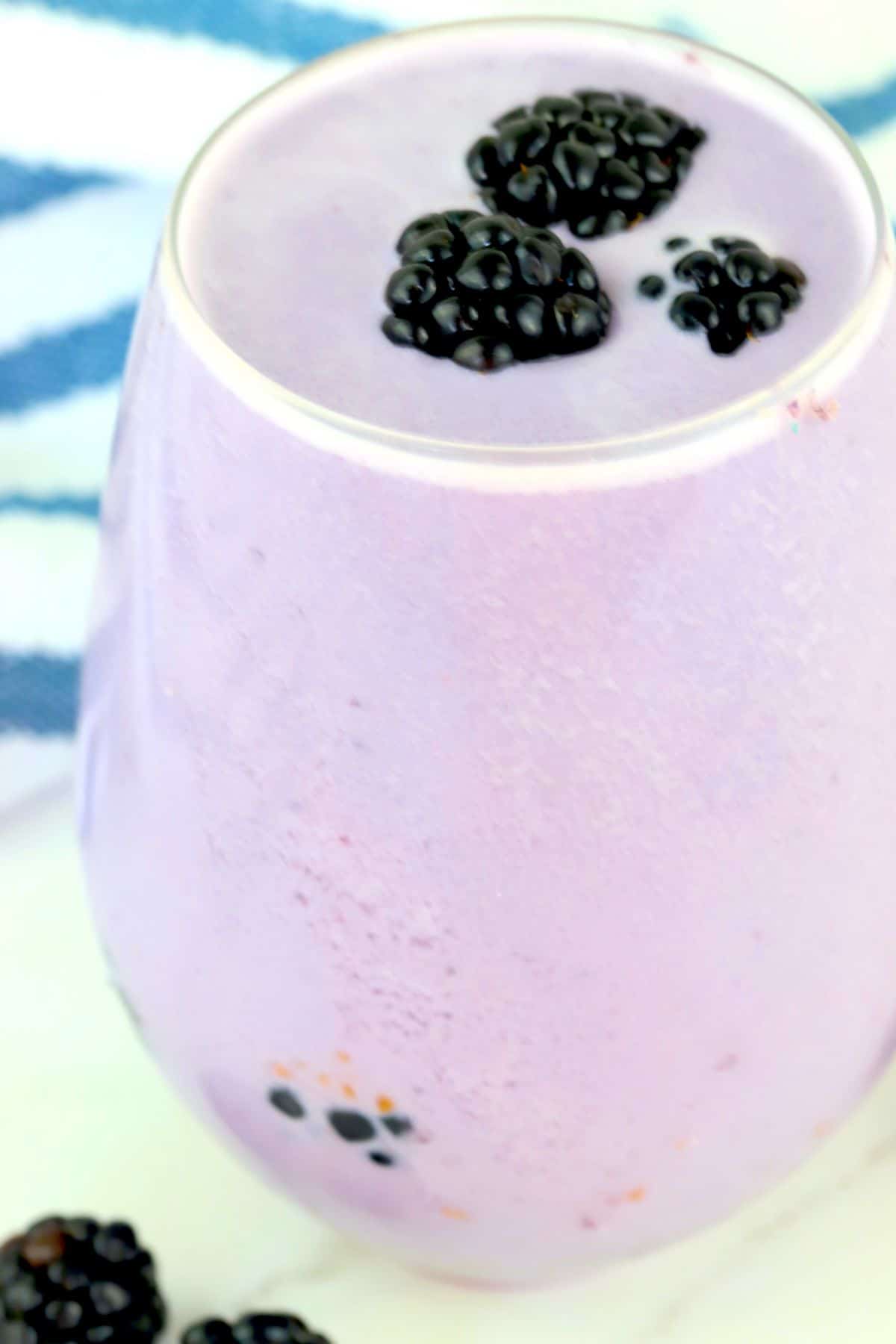 low carb blackberry smoothie in a glass with a blue and white kitchen towel.