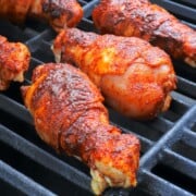 bacon wrapped chicken legs on a grill.