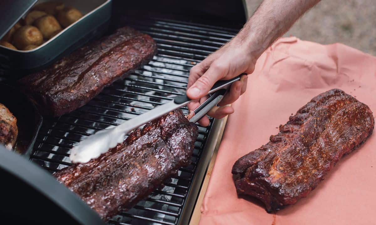 ribs on the grill being lifted with bbq tongs.