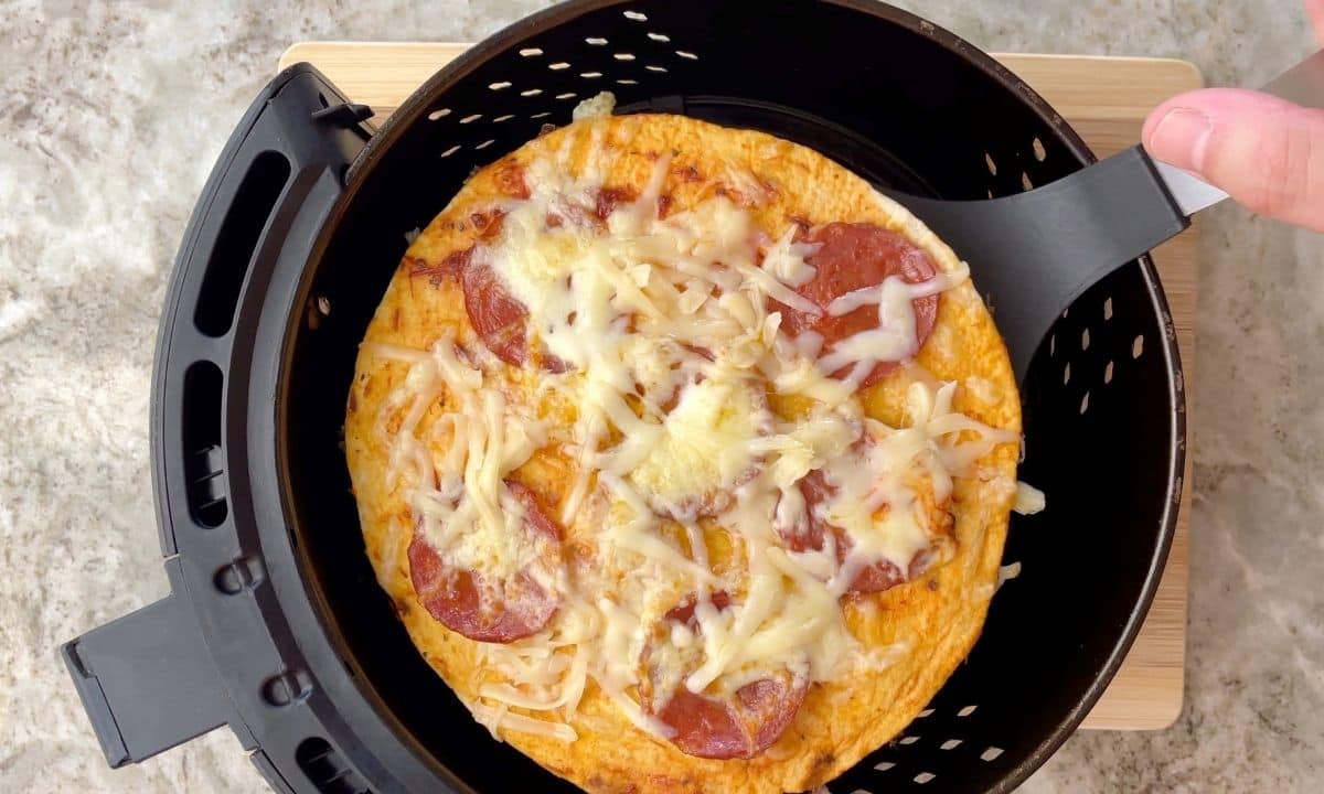 removing tortilla pizza from the air fryer basket.