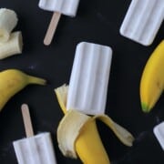 sugar free banana popsicles laying flat with black background and fresh bananas.