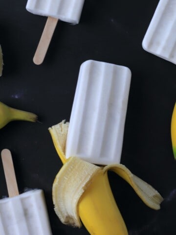 sugar free banana popsicles laying flat with black background and fresh bananas.