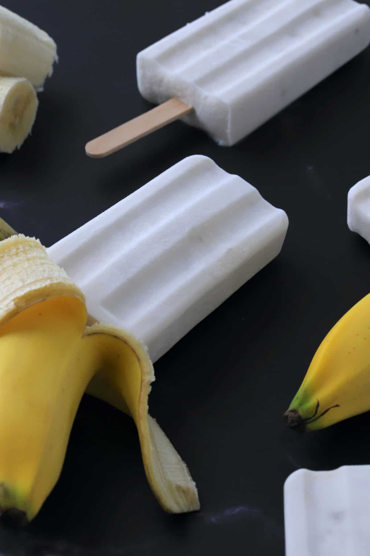 sugar free banana popsicles laying flat with black background and fresh bananas.