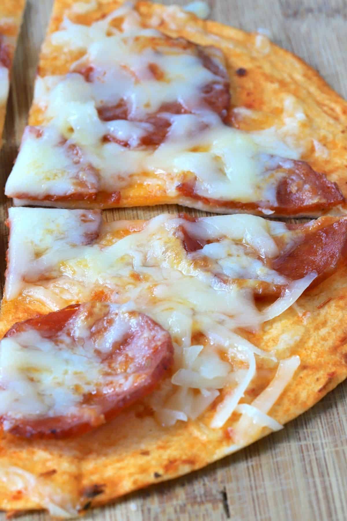 air fryer tortilla pizza topped with pepperoni and cheese on a cutting board.