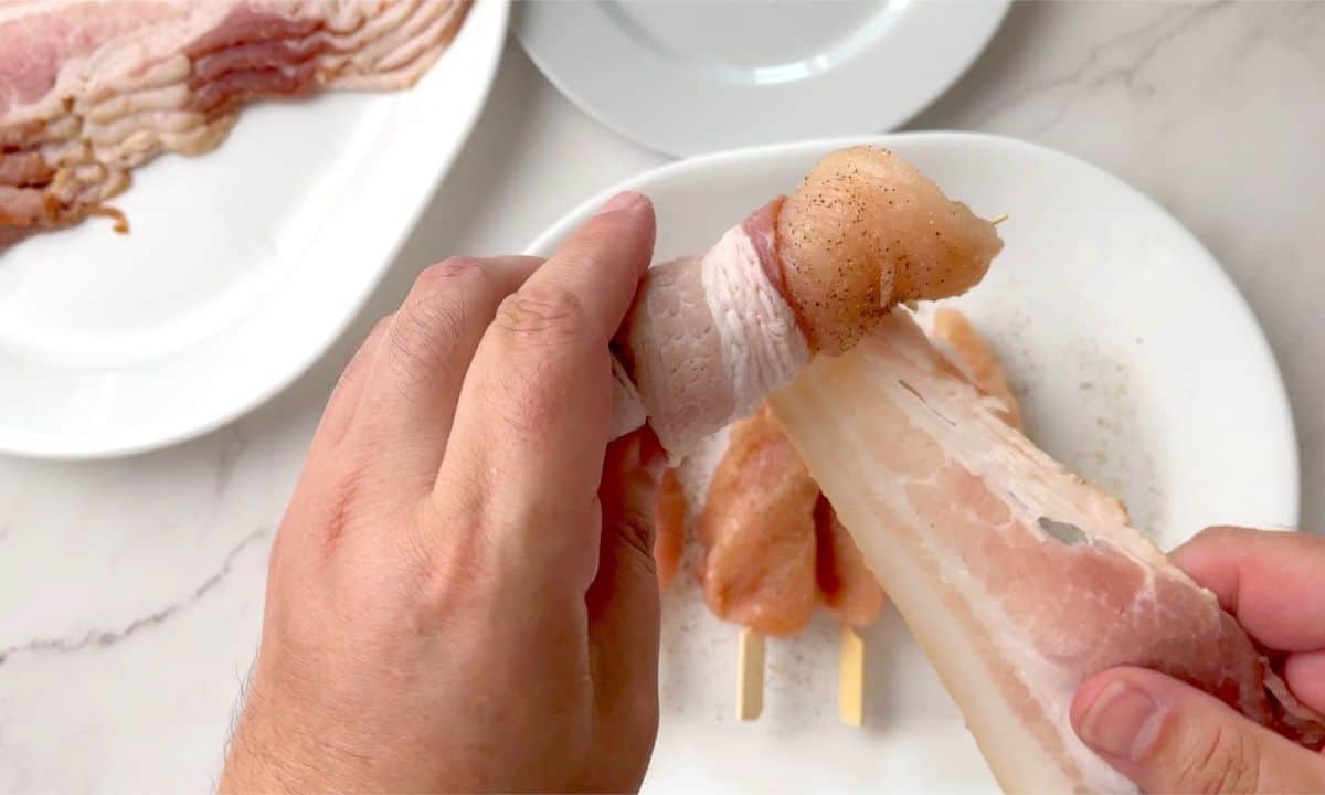 wrapping bacon around chicken on a skewer.
