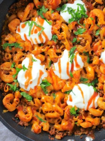 keto healthy taco pasta in a skillet topped with sour cream, taco sauce and cilantro.