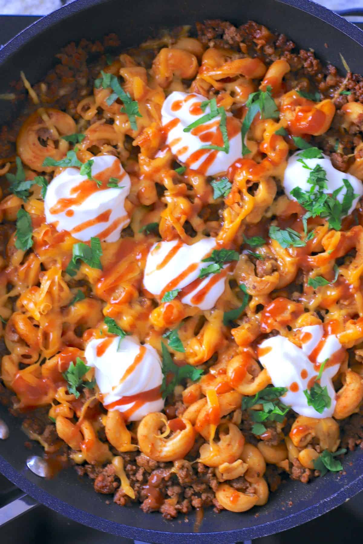skillet with taco pasta topped with sour cream, taco sauce and cilantro.