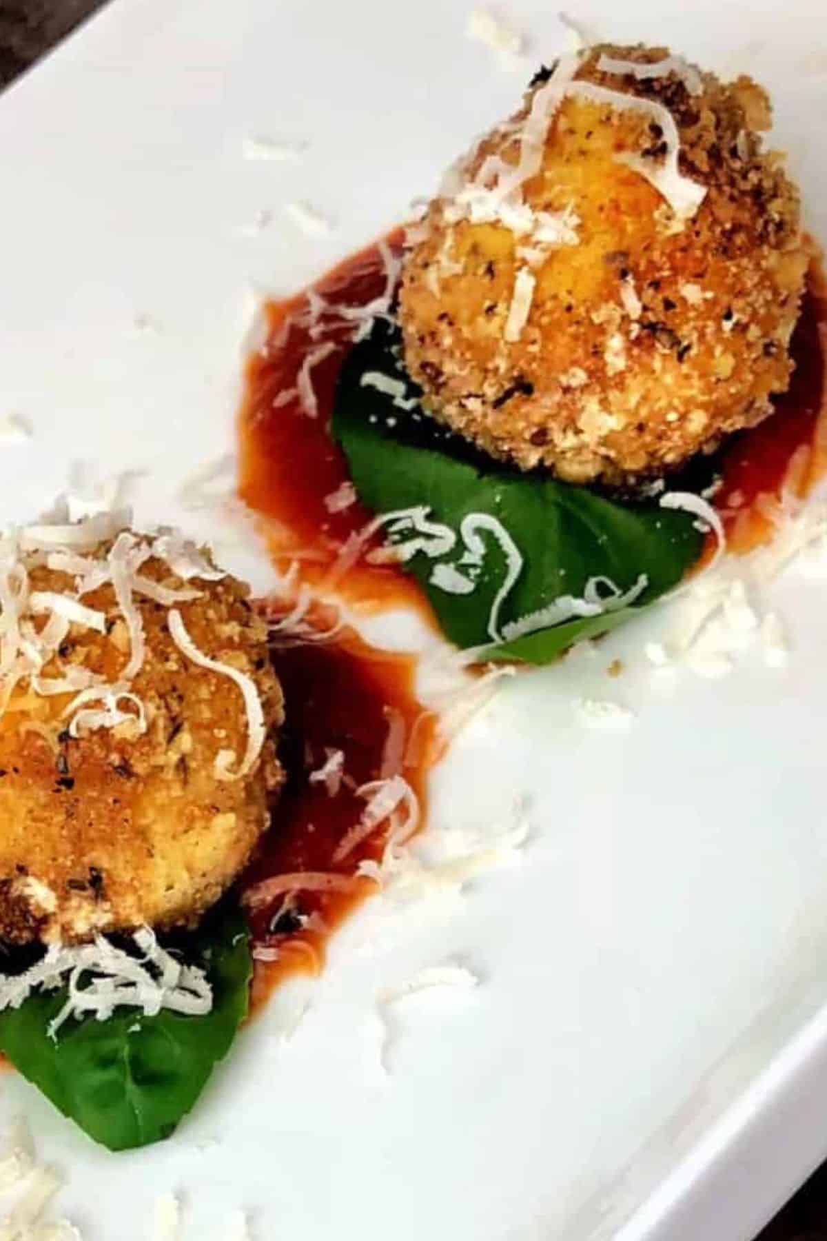 ricotta balls on tomato sauce and a basil leaf on a white plate.