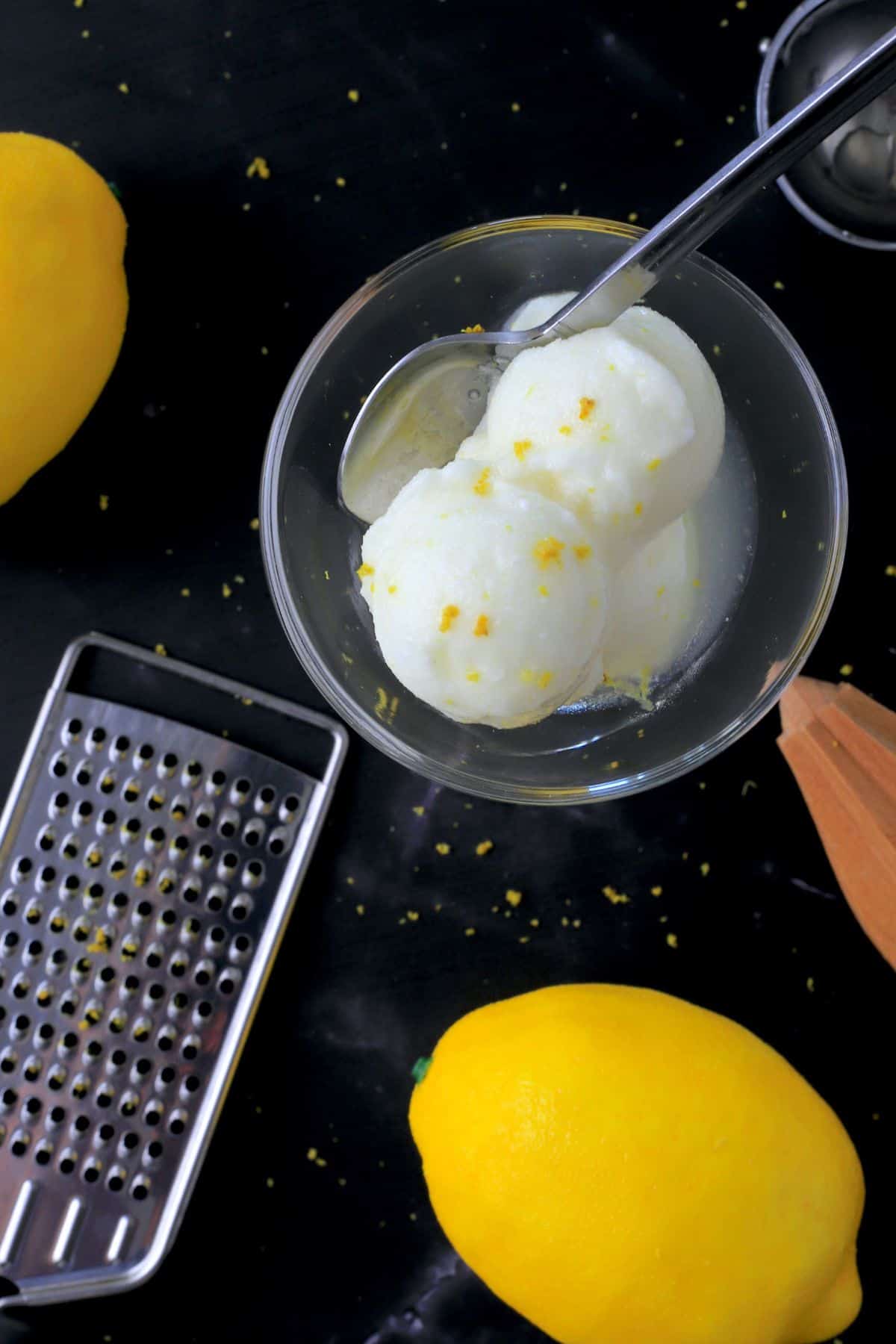 coupe glass with lemon sorbet and a spoon next to a lemon, zester and grater.