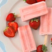 sugar free strawberry ice cream popsicles on a plate with fresh strawberries.
