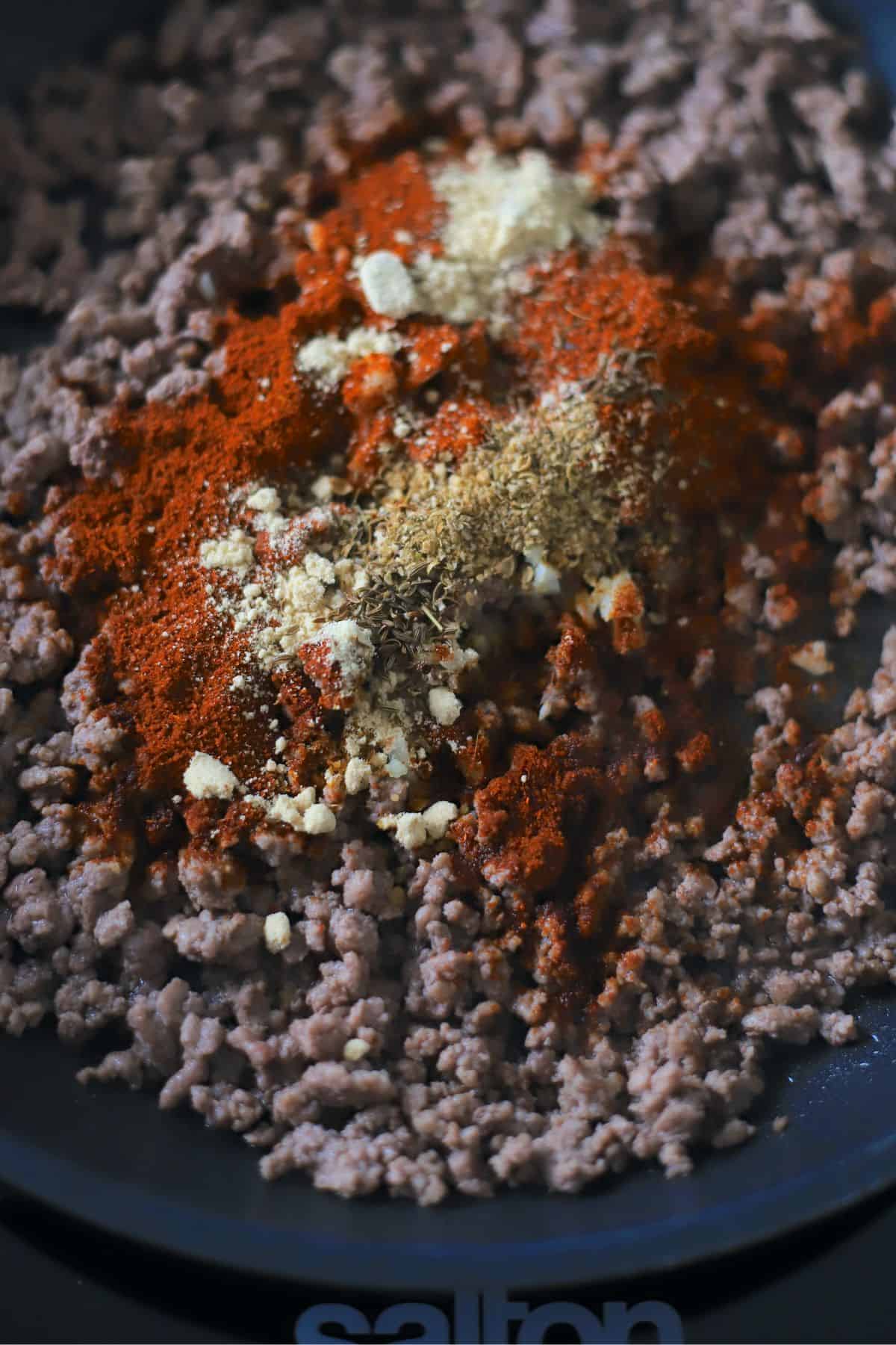 cooked ground meat in a skillet topped with seasoning spices.