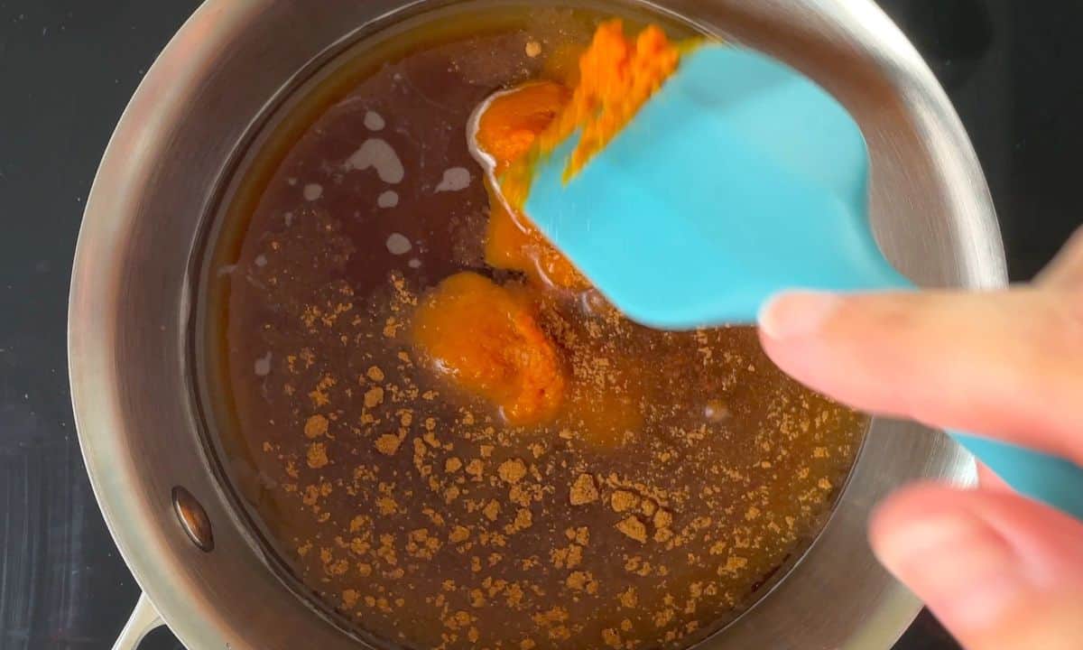 stirring ingredients in a saucepan with a blue spatula.
