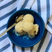 Blue bowl with butterscotch ice cream and a spoon and a blue and white striped cloth.