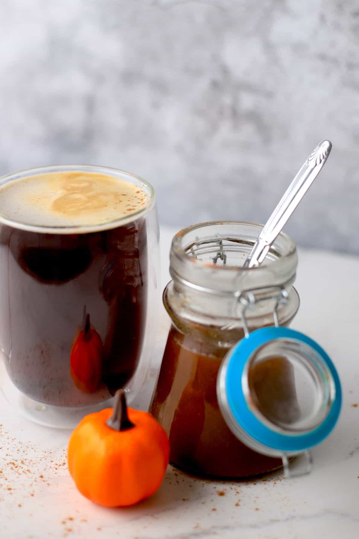 cup of black coffee with jar of sugar free pumpkin syrup on the side with pumpkin ornaments.