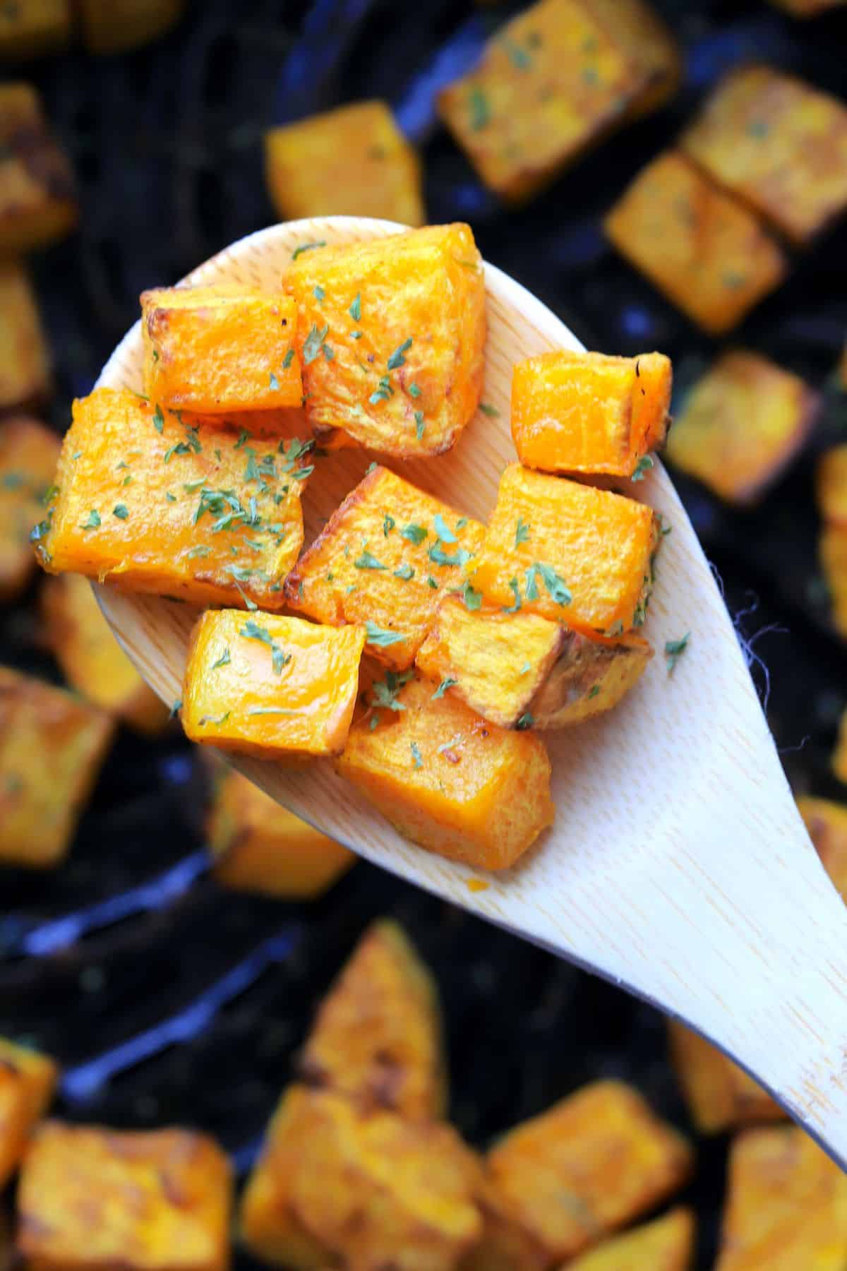 wooden spoon holding cubes of the air fried butternut squash.