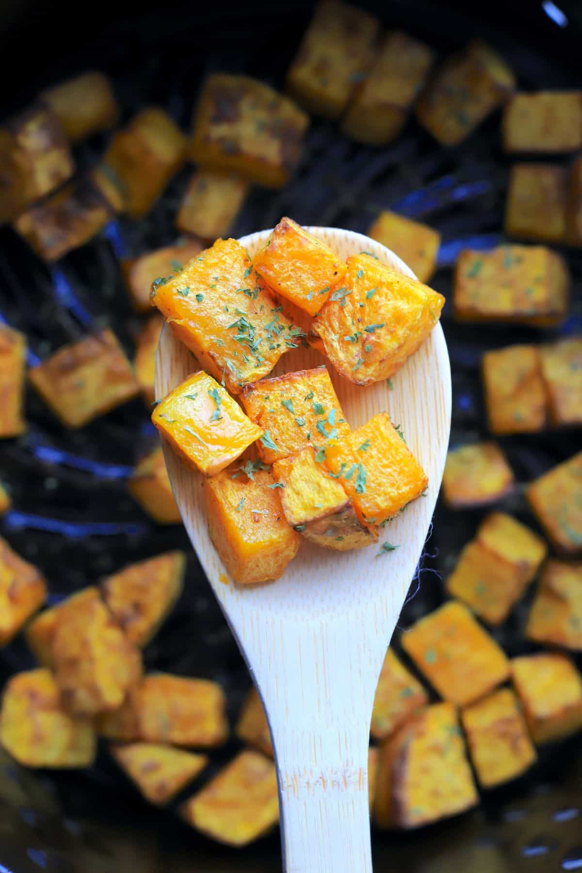 wooden spoon holding cubes of the air fried butternut squash.