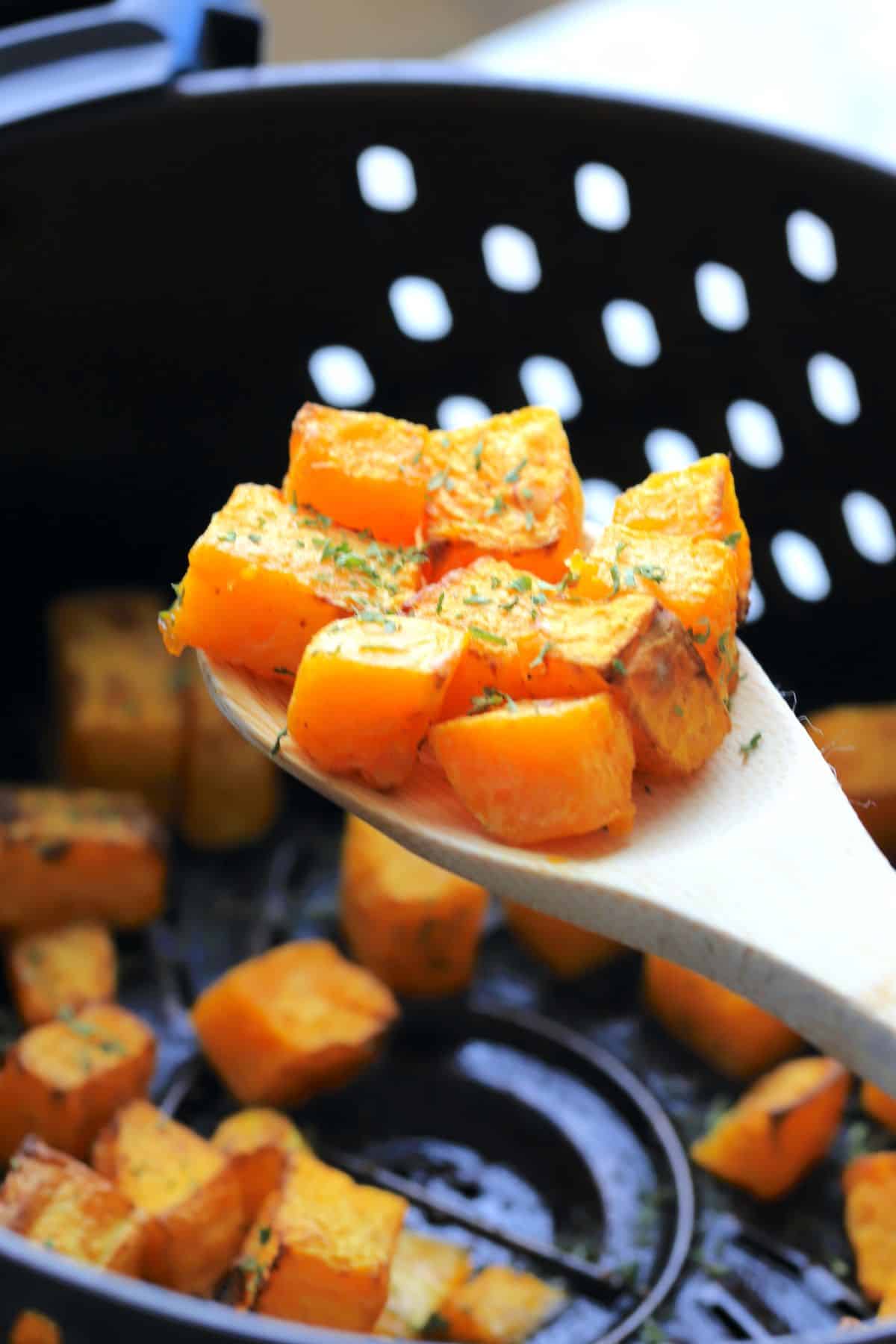 wooden spoon holding cubes of the air fried butternut squash.