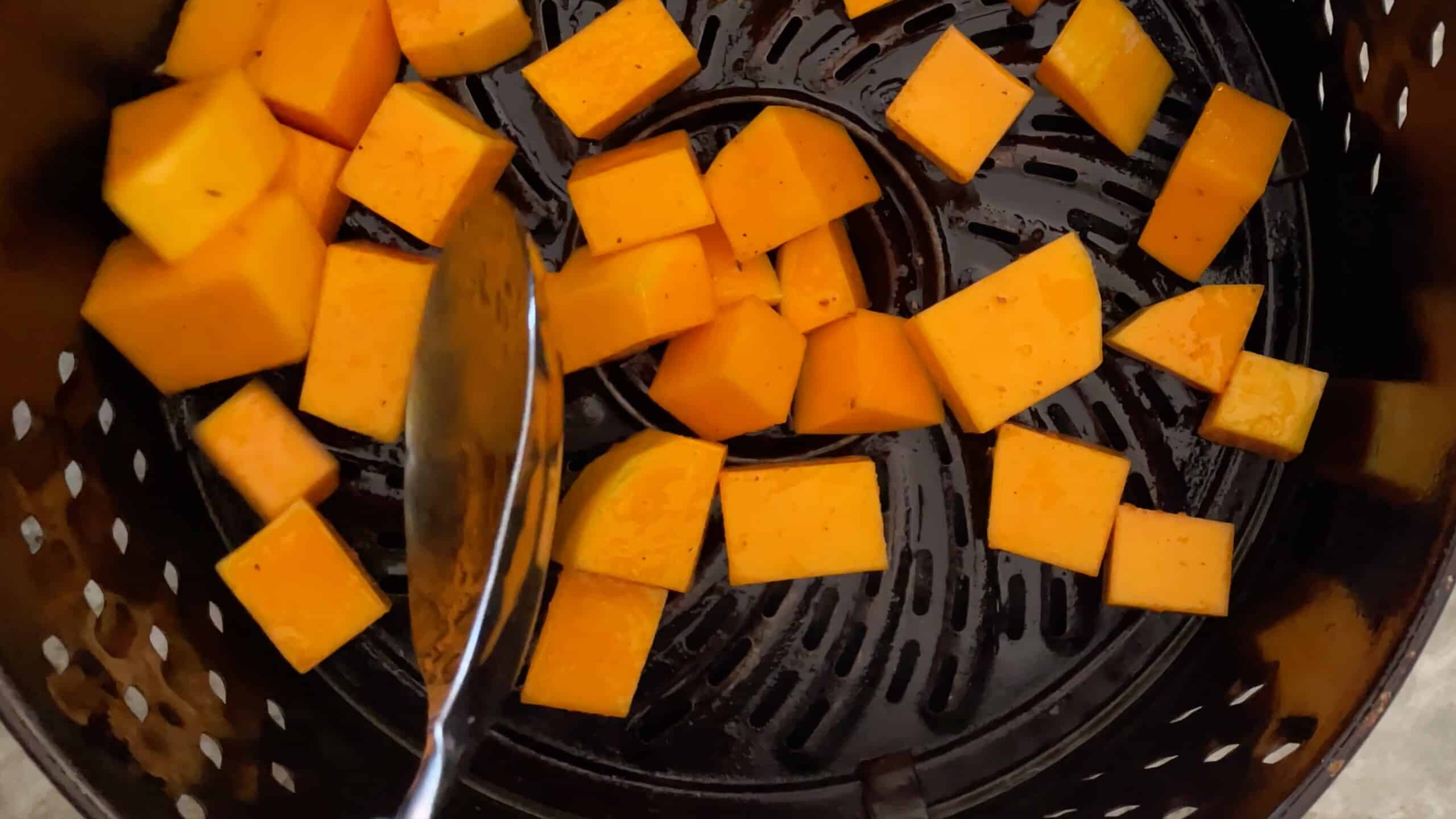 butternut squash cubes in the air fryer basket with a spoon.