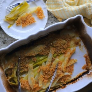 braised fennel and leeks in a white casserole dish topped with a parmesan crust with a plate on the side.