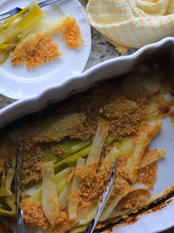 braised fennel and leeks in a white casserole dish topped with a parmesan crust with a plate on the side.