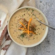 low carb roasted cauliflower soup in a white bowl topped with cheddar and flakes of parsley.