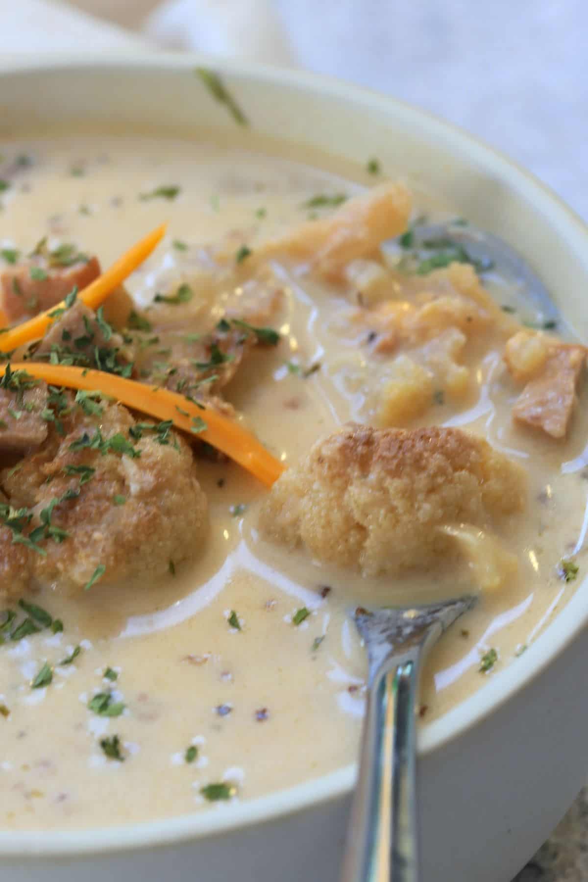 low carb roasted cauliflower soup in a white bowl topped with cheddar and flakes of parsley.